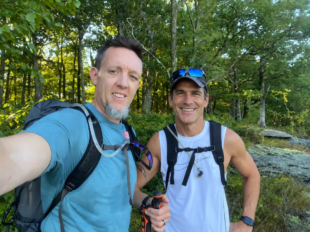 Two backpackers hiking a mountain trail together on a multi-day coaching journey
